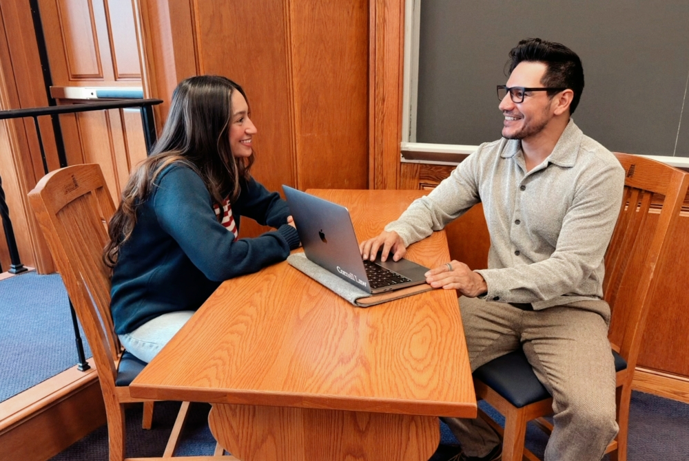 two people sitting at a table with a computer