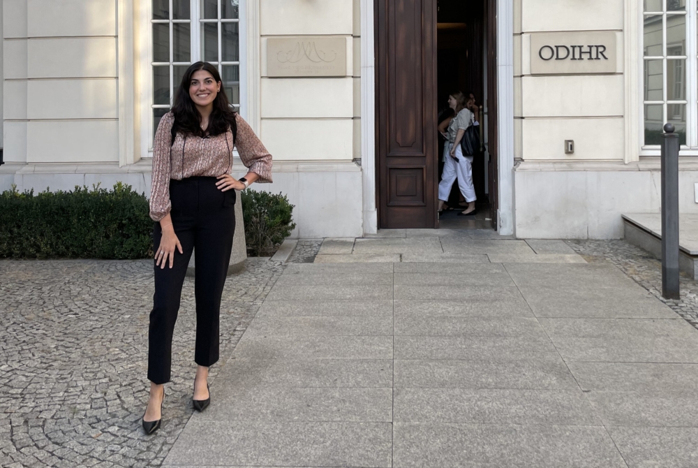 Woman standing in front of a building with a sign that says ODIHR
