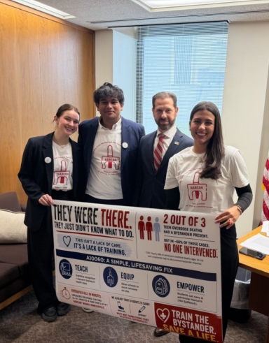 Four students holding a banner that says They Were There and other text describing Narcan use